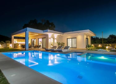 Luxury modern villa at night with a glowing swimming pool and outdoor lounge area.