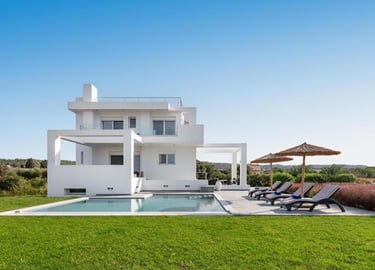 Luxury modern white villa with a private swimming pool, sun loungers, and umbrellas on a green lawn.