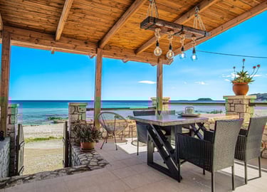 Rustic outdoor patio with wooden pergola, dining table, and ocean view in a seaside villa.