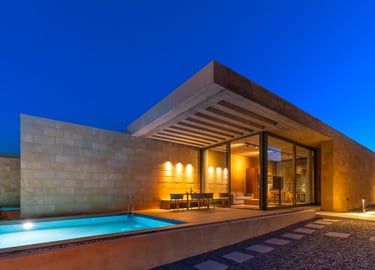 Modern luxury villa at dusk with an outdoor swimming pool, patio dining, and warm interior lighting.