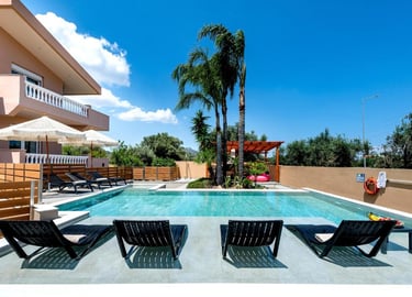 Luxury villa rental with a private swimming pool, sun loungers, and palm trees under a blue sky.