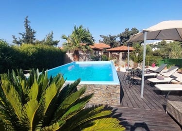 Luxury outdoor swimming pool with sun loungers and umbrella on a wooden deck.
