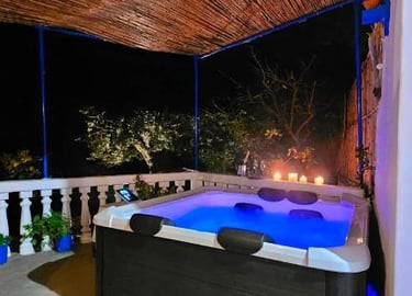 Luxury outdoor hot tub with blue LED lighting under a bamboo roof at night with candles.