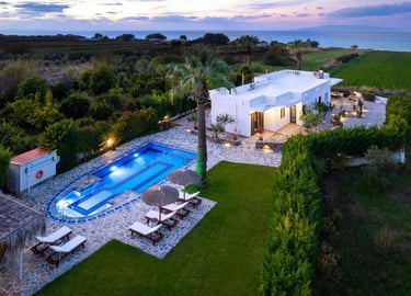Luxury white villa with swimming pool and palm trees at sunset overlooking the ocean.