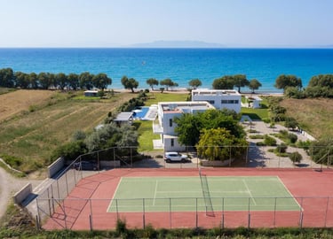 Luxury beachfront villa with a private tennis court and swimming pool overlooking the blue sea.
