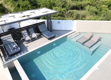 Modern luxury infinity pool with sun loungers and a pergola on a private terrace overlooking green hills.