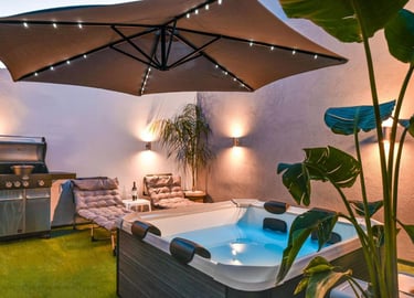 Modern outdoor patio with hot tub, gas grill, and lighted umbrella for luxury backyard relaxation.