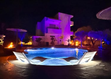 Luxury villa with swimming pool at night featuring purple ambient lighting and lounge chairs.