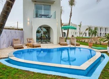 Luxury villa with heart-shaped swimming pool, lounge chairs, and palm trees at a tropical resort.