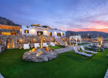 Luxury villa in Rhodes with lit patio, lawn seating, and sunset mountain views.