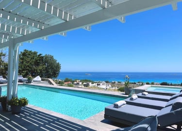 Luxury infinity pool with sun loungers overlooking the blue Mediterranean sea under a white pergola.