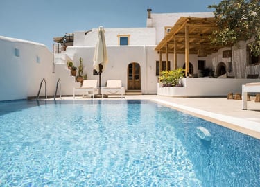 Luxury Greek villa with a private turquoise swimming pool, lounge chairs, and Cycladic architecture.