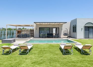 Luxury villa with a private swimming pool, sun loungers on a green lawn, and an outdoor dining area.