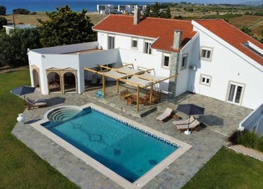 Luxury white villa with red tile roof featuring a private swimming pool, patio, and ocean view.