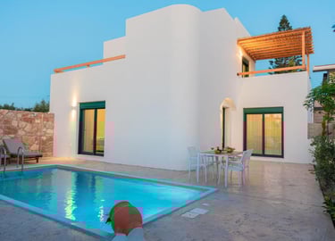 Luxury white villa with a private swimming pool and patio dining area at dusk.