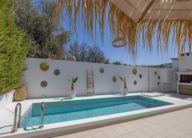 Luxury villa terrace with a private swimming pool, white walls, and bohemian style decor under a clear blue sky.
