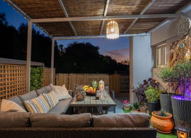 Cozy outdoor patio at dusk with a sectional sofa, rattan lighting, and garden decor.