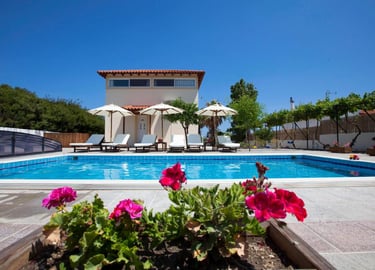 Luxury vacation villa with private swimming pool, sun loungers, and umbrellas under a clear blue sky.