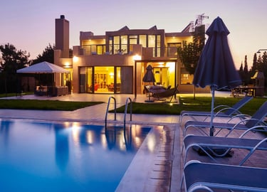 Luxury modern villa with a lighted swimming pool and lounge chairs at sunset.