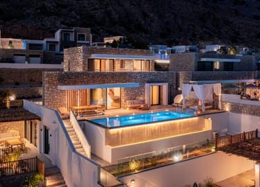 Luxury stone villas with a private infinity pool illuminated at night on a Greek hillside.
