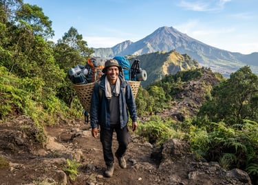 A local Indonesian mountain porter smiling, wearing professional outdoor gear, carrying a neatly packed traditional bamboo basket with modern hiking backpacks, Mount Rinjani volcanic ridge in the background, bright crisp morning light.