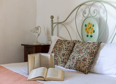 Cozy bedroom with open books on a bed featuring floral pillows and a vintage metal headboard.