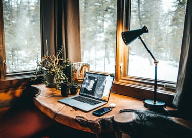 Cozy home office desk with laptop and lamp overlooking a snowy winter forest.