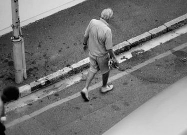 Black-and-white photo of a man walking along a city curb, from Martin Osner’s “On the Move” collection.