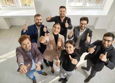 Grupa uśmiechniętych ludzi patrząca w górę i pokazująca kciuk do góry
