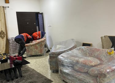 Two professional movers in orange high-visibility jackets with reflective strips collaborate to lift