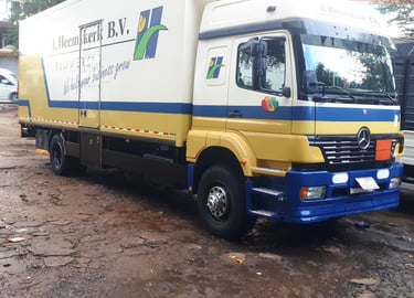 A yellow and blue Mercedes-Benz delivery truck branded "A. Heemskerk B.V." with green flower motifs