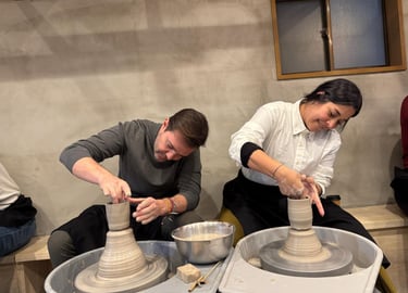 A man and woman shaping clay on spinning pottery wheels during a professional ceramics class.