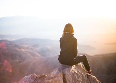 Femme assise au sommet d'une montagne qui regarde la vue