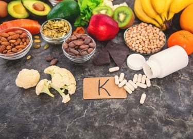 Variety of Vitamin K food sources including leafy greens, nuts, and fruit alongside supplement capsules.