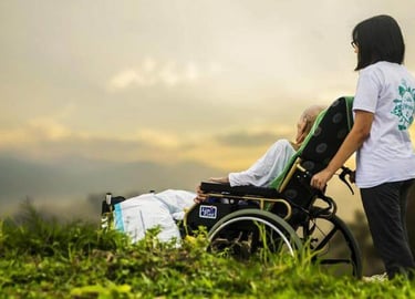 Caregiver pushing an elderly person in a wheelchair outdoors at sunset.