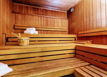 Traditional wooden cedar sauna room with tiered benches, bucket, ladle, and rolled white towels.