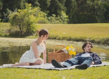 a man and woman sitting on a blanket in the grass