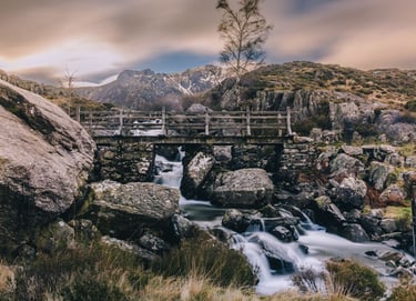 Rustic wooden bridge over a cascading waterfall in the rocky Snowdonia mountain landscape.