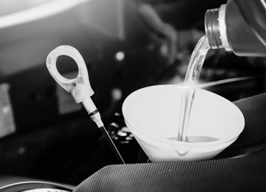 Pouring fresh synthetic motor oil through a funnel into a car engine during a routine oil change.