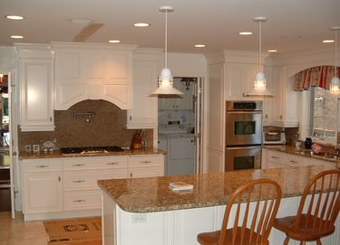 A spacious, brightly lit kitchen with white cabinets, granite countertops, stainless steel appliances, and a central island