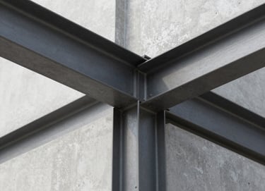 An architectural detail shot focusing on the intersection of steel and concrete. The lighting is clean and professional, highlighting the textures of #6B6760 metal and the smooth #FBF9F6 concrete surfaces. Modern and precise composition.