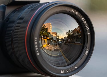 Close up shot of a professional camera lens reflecting a blurred, vibrant Latin American / Hispanic urban scene at golden hour, sophisticated and sharp.