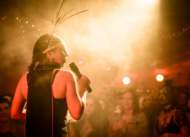 A singer in an avant-garde headpiece performs live on a smoky stage for a crowd.