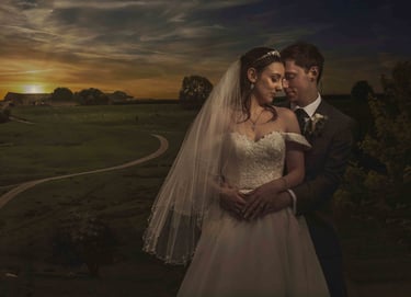Newlywed couple posing for a romantic wedding portrait in front of a rural sunset landscape.