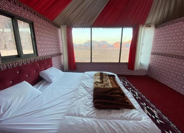 a bed with a red blanket and a bed in a tent
