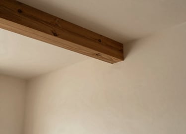 An interior architectural shot focusing on a single wooden beam and a plastered wall. The lighting is diffuse and warm (#7C4E3A), creating a philosophical and quiet atmosphere. Clean lines, ample whitespace.
