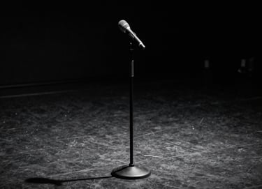 An elegant, minimalist image of a classic microphone stand on a dark, empty stage, dramatic top lighting creating long shadows, deep anthracite and charcoal tones.