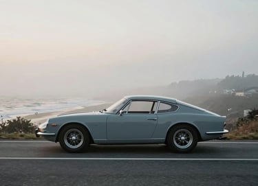 A side profile of a 1960s classic sports car driving through a misty coastal road at dawn. The colors are muted #5D6D7E blues and #B2BEB5 grays, emphasizing a timeless, cinematic aesthetic.