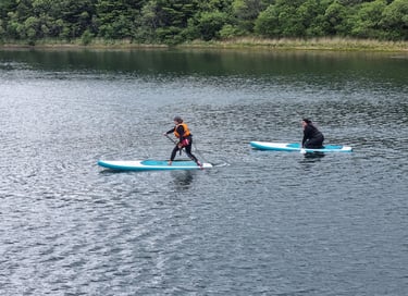 A stand up paddle board instructor demonstrating a step back turn while a student watches