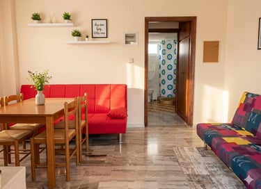 Modern studio apartment featuring a red sofa, wooden dining set, and colorful patterns.